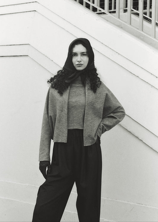Person wearing a gray sweater and dark pants against a white background