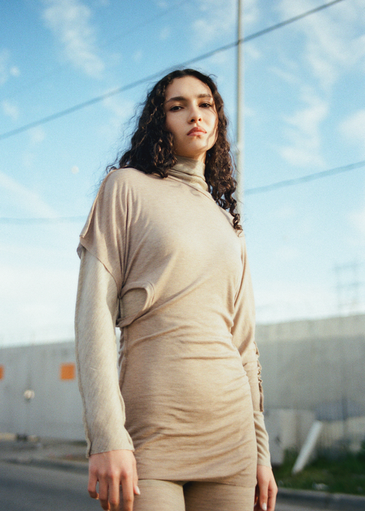 Woman wearing a beige outfit standing outdoors with a clear sky.